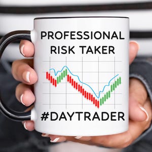May include: White ceramic mug with a black handle and rim, featuring the text "PROFESSIONAL RISK TAKER" above a stock market graph with red and green bars, and the hashtag "#DAYTRADER" below.