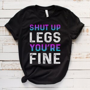 May include: Black t-shirt with the text "Shut Up Legs You're Fine" in white with a distressed look. The text "You're" is in blue and purple.