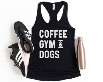 May include: Black tank top with white text that reads "COFFEE GYM & DOGS". The tank top is laying flat on a white surface with a pair of black and white sneakers and a rose gold water bottle.