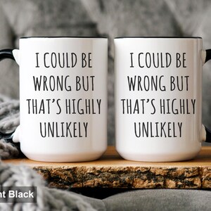 May include: Two white ceramic mugs with black handles and rims. Each mug has the text "I COULD BE WRONG BUT THAT'S HIGHLY UNLIKELY" in black. The mugs are on a wooden surface.