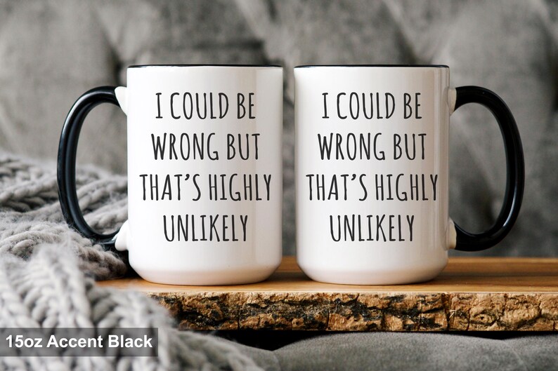 May include: Two white ceramic mugs with black handles and rims. Each mug has the text "I COULD BE WRONG BUT THAT'S HIGHLY UNLIKELY" in black. The mugs are on a wooden surface.