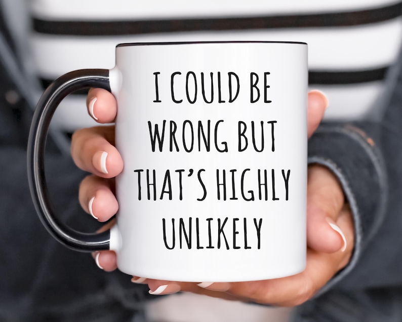 May include: White ceramic mug with a black interior and handle. The mug features the text "I COULD BE WRONG BUT THAT'S HIGHLY UNLIKELY" in black, centered on the front. The mug is held by a person.