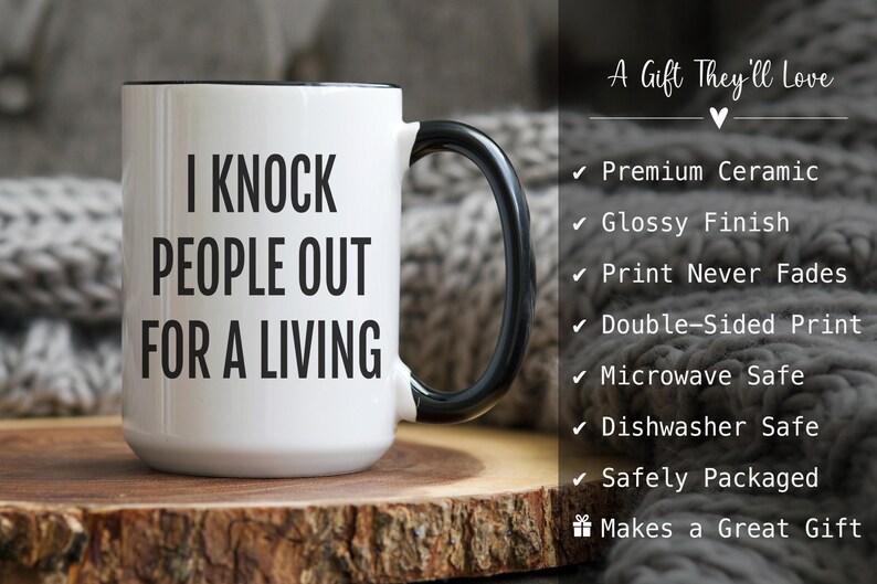 May include: White ceramic mug with a black handle and rim. The mug features the text "I KNOCK PEOPLE OUT FOR A LIVING" in bold black letters. The mug is on a wooden surface.