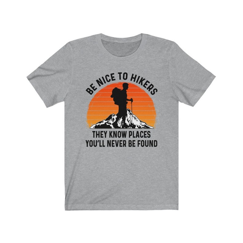 Op de afbeelding: Grijs T-shirt met een silhouet van een wandelaar voor een zonsondergang. De tekst luidt "Wees aardig tegen wandelaars, ze kennen plekken waar je nooit gevonden zult worden."