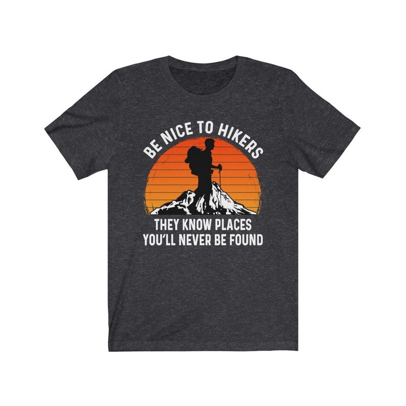 Op de afbeelding: Een donker grijs gem&ecirc;leerd t-shirt met een witte afbeelding van een wandelaar met een rugzak en een bergketen op de achtergrond. De tekst "Be Nice To Hikers They Know Places You'll Never Be Found" staat op het t-shirt gedrukt.