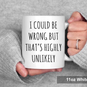 May include: White ceramic mug with the text "I COULD BE WRONG BUT THAT'S HIGHLY UNLIKELY" in black. The mug is held by a person wearing a gray sweater. The mug is labeled "11oz White".
