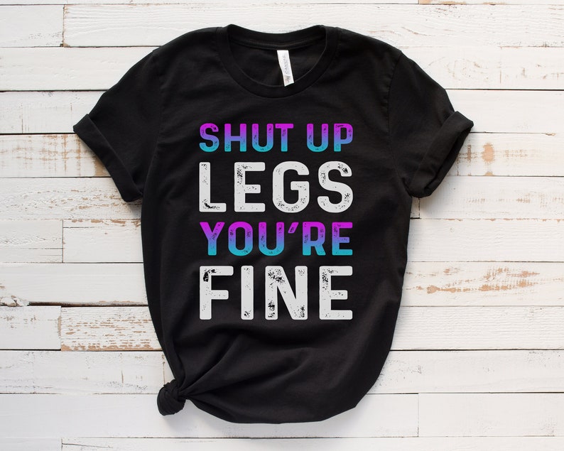 May include: Black t-shirt with the text "Shut Up Legs You're Fine" in white with a distressed look. The text "You're" is in blue and purple.