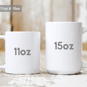 May include: Two white ceramic mugs, one labeled "11oz" and the other "15oz". The mugs are displayed on a rustic wooden surface. The image also includes the text "Available in 11oz & 15oz".