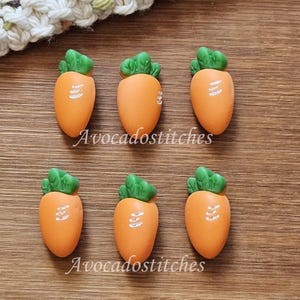 May include: Six orange carrot-shaped buttons with green tops. The buttons have white lines on them.