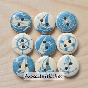 Peut inclure: Neuf boutons en bois sur le thème nautique avec des motifs bleus et blancs. Les boutons présentent des images de voiliers, d'une roue de navire, d'une rose des vents, d'une bouée de sauvetage et d'une ancre. Le texte "AvocadoStitches" est visible.
