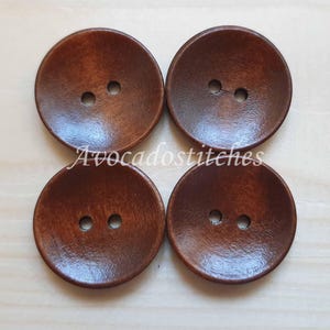 May include: Four brown wooden buttons with two holes each. The buttons are round and have a slightly raised center.