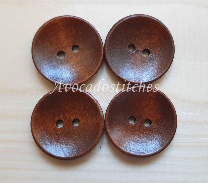 May include: Four brown wooden buttons with two holes each. The buttons are round and have a slightly raised center.