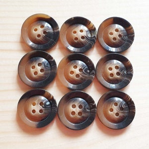 Peut inclure: Neuf boutons marbrés brun et noir avec six trous chacun.