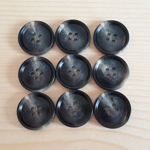 May include: A set of nine round, dark grey buttons arranged in a three-by-three grid. Each button features a four-hole centre design and a subtle, swirling marbled pattern in lighter grey tones across the surface of the circular rim.