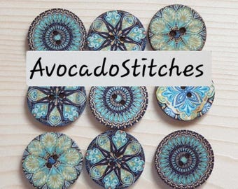 May include: Nine round buttons arranged in a grid, each featuring distinct blue, teal, and gold geometric or floral patterns. Each button has two central holes. The text "AvocadoStitches" is overlaid across the center of the image.
