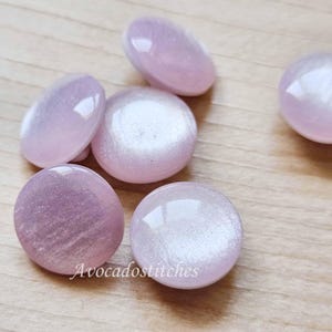 May include: Six iridescent pink and white buttons with a pearlescent finish. The buttons are round and have a smooth surface.