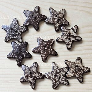 May include: Eight brown coconut shell star-shaped buttons with two holes each. The buttons have a natural, rustic look and are perfect for adding a touch of coastal charm to your crafts.