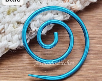 Könnte beinhalten: Ein leuchtend blauer Spiral-Maschenmarkierer aus Metall mit glatter, glänzender Oberfläche. Das Spiraldesign besteht aus einem durchgehenden Draht, der sich zur Mitte hin einrollt. Der Text "Blue" steht in einem weißen Feld und "AvocadoStitches" ist sichtbar.
