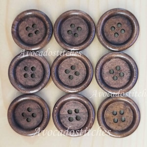 Peut inclure: Neuf boutons ronds en bois brun foncé, chacun avec quatre trous, disposés en grille. Les boutons présentent un aspect texturé et un grain de bois naturel. Le texte "Avocadostitches" est visible. Idéal pour la couture.