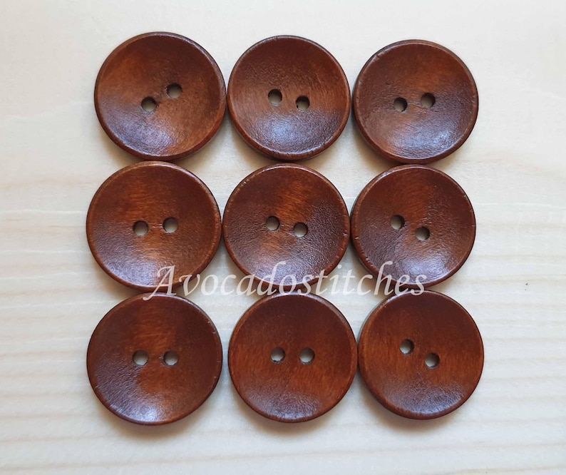 May include: Nine brown wooden buttons with two holes each. The buttons are round and have a slightly raised center.