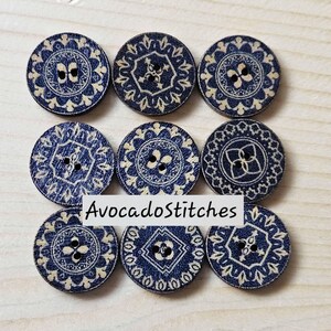 May include: Nine circular wooden buttons arranged in a three-by-three grid, each featuring a dark blue base with intricate cream-coloured geometric and floral patterns. The text AvocadoStitches is overlaid across the centre of the image.