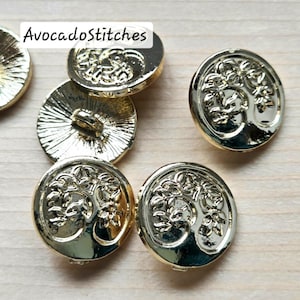Peut inclure: Boutons métalliques dorés avec un motif d'arbre de vie. Les boutons sont ronds et ont une finition brillante. Le texte "AvocadoStitches" est visible sur l'un des boutons.