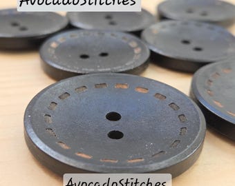 May include: A collection of dark gray, round buttons with two holes and a decorative stitched border. The buttons have a slightly textured surface and are arranged on a light-colored surface. The text "AvocadoStitches" is displayed on the image.