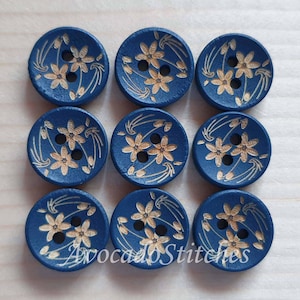 Peut inclure: Un ensemble de neuf boutons ronds bleus disposés en une grille de trois par trois. Chaque bouton présente un design à deux trous et est gravé d'un motif floral clair composé de petites fleurs et de lignes courbes. Le texte AvocadoStitches est visible.