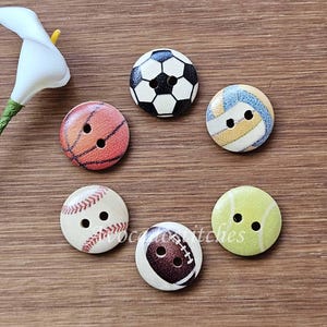 May include: Six round wooden buttons featuring printed sports ball designs, including a football, basketball, volleyball, baseball, tennis ball, and American football. Each button has two central holes for sewing and a smooth, flat surface finish.