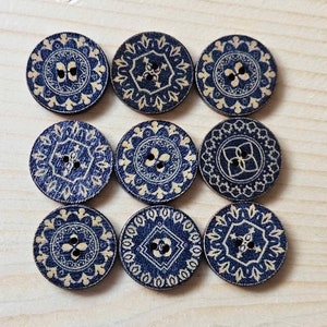 May include: Nine round wooden buttons with a blue background and a gold design. The buttons have two holes each.