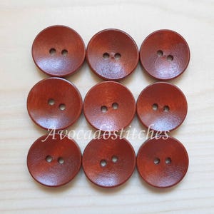 May include: Ten brown wooden buttons with two holes each. The buttons are round and have a slightly raised centre.