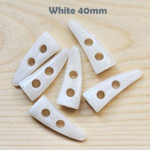 May include: White plastic buttons shaped like a horn with two holes. The buttons are 40mm long. White 40mm.