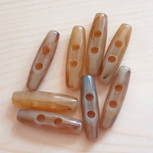 May include: Eight brown and beige plastic toggle buttons with two holes each.