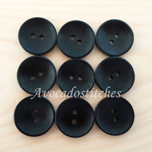 May include: Eight black wooden buttons with two holes each. The buttons are round and have a slightly raised centre.