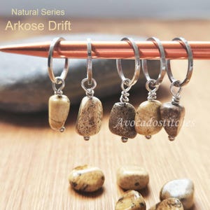 May include: Set of five natural stone stitch markers with silver rings. The stones are a light brown with darker brown markings. The text "Natural Series Arkose Drift" is visible at the top of the image.