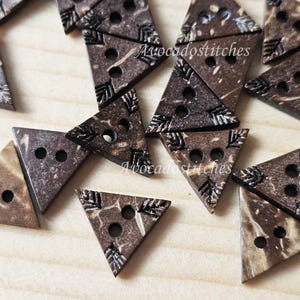 May include: A collection of brown triangle-shaped coconut shell buttons with two holes each. The buttons have a natural wood grain pattern and are decorated with a carved design.