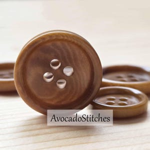 May include: Close-up of several brown buttons with four holes each. The buttons have a glossy finish and a wood-grain appearance. The text "AvocadoStitches" is visible on the image.