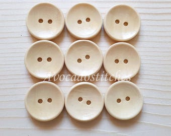 May include: Ten round, wooden buttons with two holes each. The buttons are a light beige color.