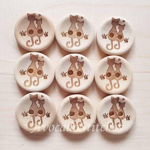 May include: Set of 8 wooden buttons featuring a pair of cats with hearts. The buttons are light brown with a dark brown design.