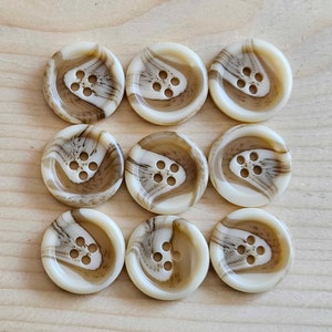May include: A set of nine round buttons arranged in a three-by-three grid. Each button features a cream-coloured base with swirling brown marbled patterns and four holes in the centre for attachment. The buttons have a smooth, glossy finish.