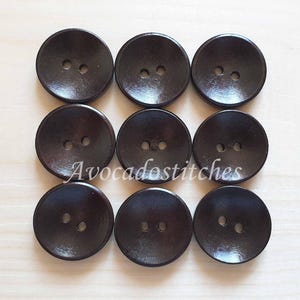 May include: Eight dark brown wooden buttons with two holes each. The buttons are round and have a slightly raised centre.