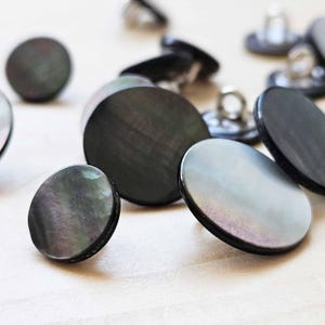 May include: A collection of black and iridescent shell buttons. The buttons are round and have a smooth, polished finish.