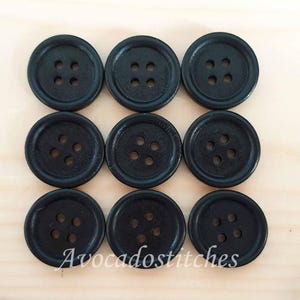 May include: A set of nine round, black buttons arranged in a three-by-three grid. Each button features a raised outer rim and four centred holes for attachment. The text "Avocadostitches" is printed in white script across the bottom row of buttons.