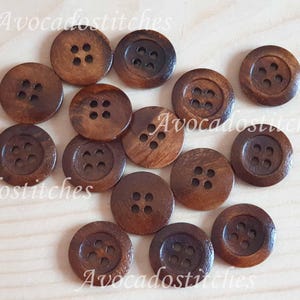 May include: A selection of round, dark brown wooden buttons, each with four holes. The buttons are displayed on a light-coloured wooden surface. The buttons have slight variations in colour and grain.