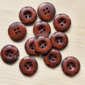 May include: A collection of eleven round, dark brown wooden buttons with four central holes. Most buttons feature a scalloped, flower-like edge, while two are smooth and circular. The text "AvocadoStitches" is visible across the buttons.