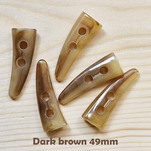 May include: Five dark brown plastic buttons shaped like horns with two holes each. The buttons are approximately 49mm long.
