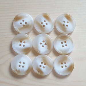 May include: Nine white buttons with a brown swirl pattern. Each button has four holes.