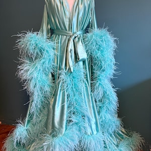 May include: A light blue satin robe with long sleeves and a sash. The robe has a feather trim around the sleeves and hem.