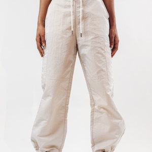 K&ouml;nnte beinhalten: Eine beige Cargohose mit Kordelzugbund und lockerer Passform. Die Hose hat zwei gro&szlig;e Seitentaschen und ist aus leichtem Stoff gefertigt.