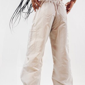 K&ouml;nnte beinhalten: Eine beige Cargohose mit Kordelzugbund und mehreren Taschen. Die Hose ist aus einem leichten, geknitterten Stoff.